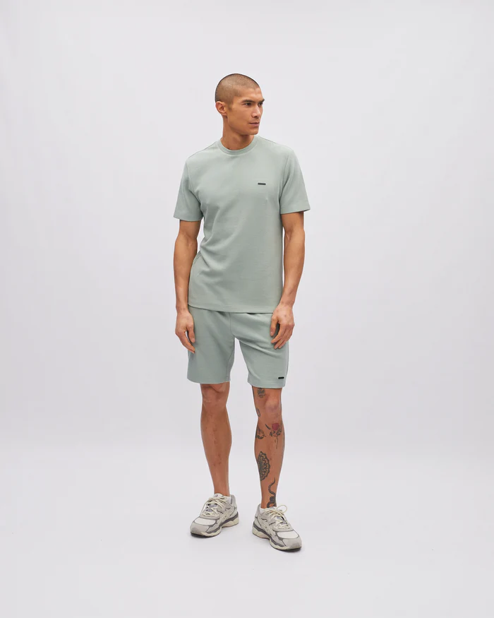 Man wearing a light green t-shirt and shorts set on a white background