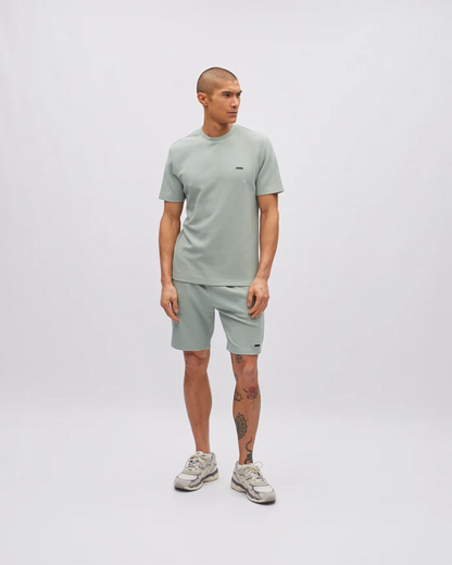 Man wearing a light green t-shirt and shorts set on a white background