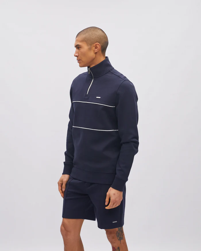 Man wearing a navy tracksuit with white stripes on a light gray background