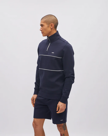 Man wearing a navy tracksuit with white stripes on a light gray background