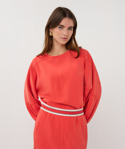 Woman wearing a coral outfit with a white belt against a plain background