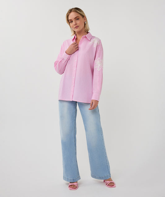 Woman wearing a pink blouse with floral patterns and light blue jeans on a white background