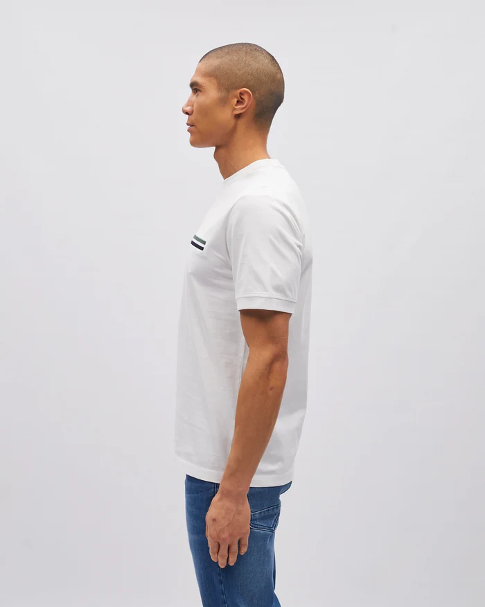 Man wearing a white t-shirt with a small logo on a plain background