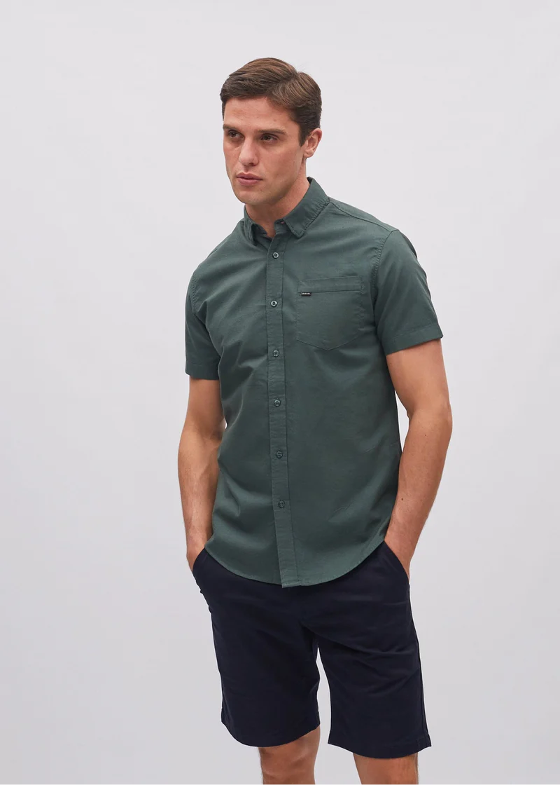 Man wearing a green short-sleeve shirt and navy shorts on a white background