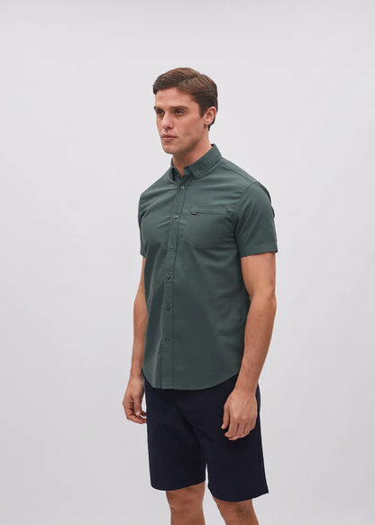Man wearing a green button-up shirt and navy shorts against a white background