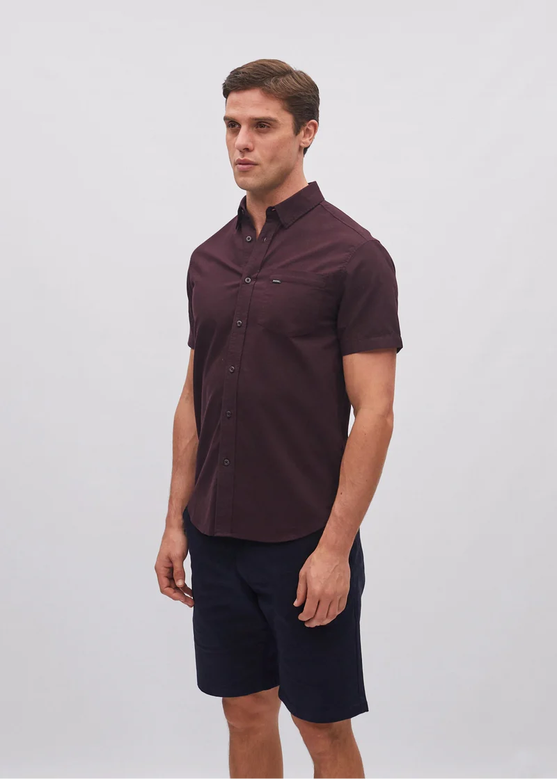 Man wearing a dark brown button-up shirt and navy shorts on a light gray background