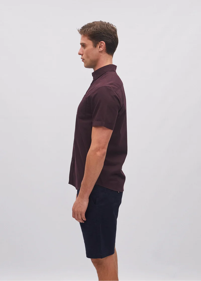 Man wearing a maroon polo shirt and black shorts on a light gray background