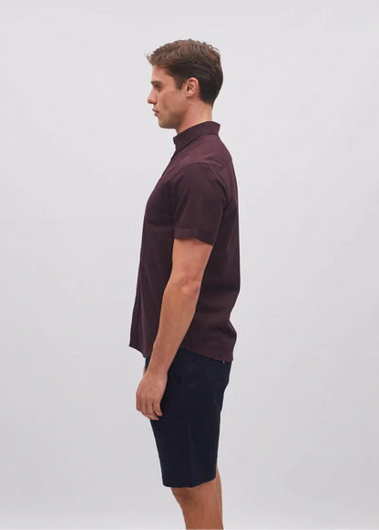 Man wearing a maroon polo shirt and black shorts on a light gray background
