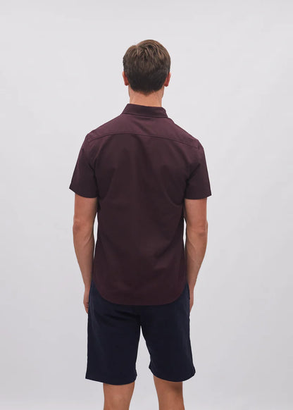 Man wearing a dark brown polo shirt and navy shorts on a white background