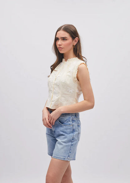 Woman wearing a white sleeveless top and denim shorts on a plain background