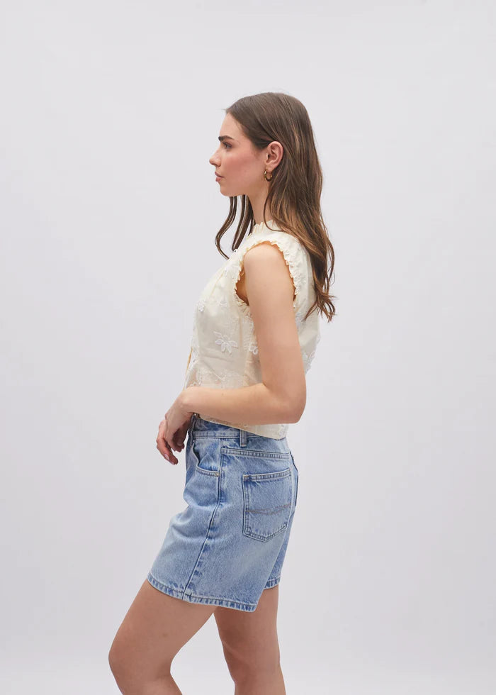 Woman wearing a white sleeveless top and denim skirt on a plain background
