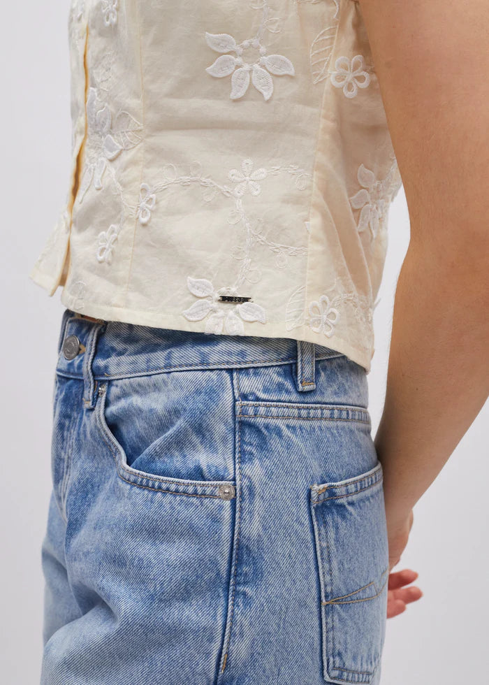 Close-up of a person wearing a beige embroidered top and blue jeans on a white background