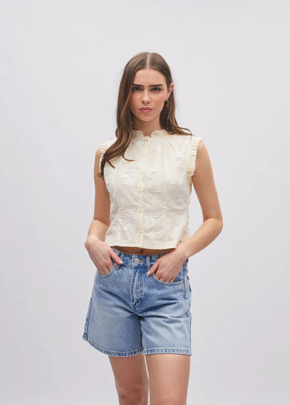 Woman wearing a white sleeveless top and denim shorts on a plain background