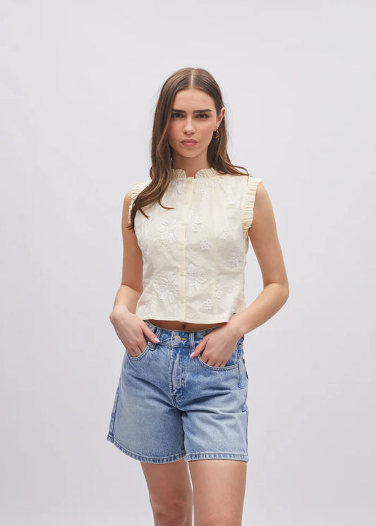 Woman wearing a white sleeveless top and denim shorts on a plain background
