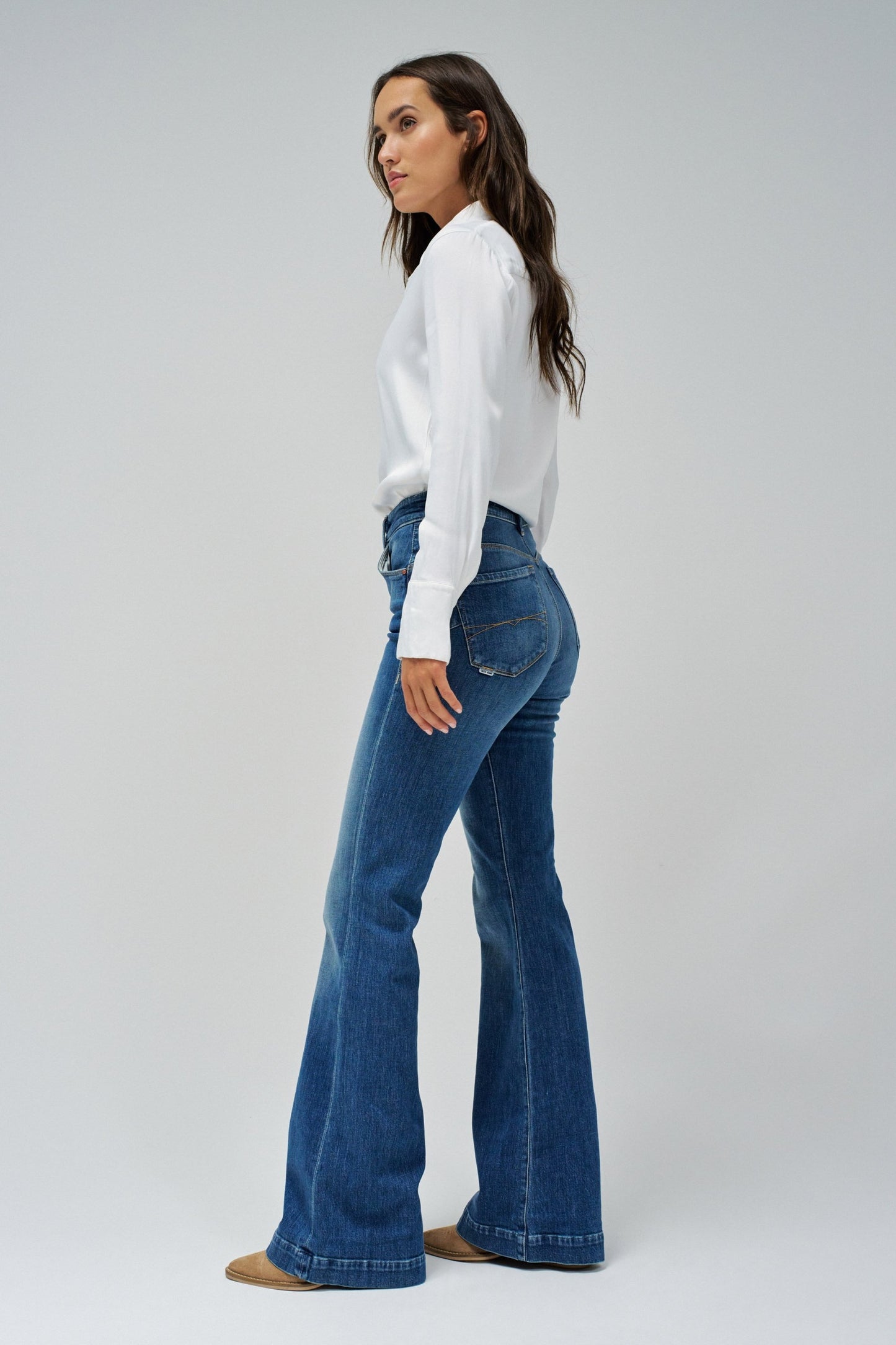 Woman wearing blue flared jeans and a white shirt on a gray background