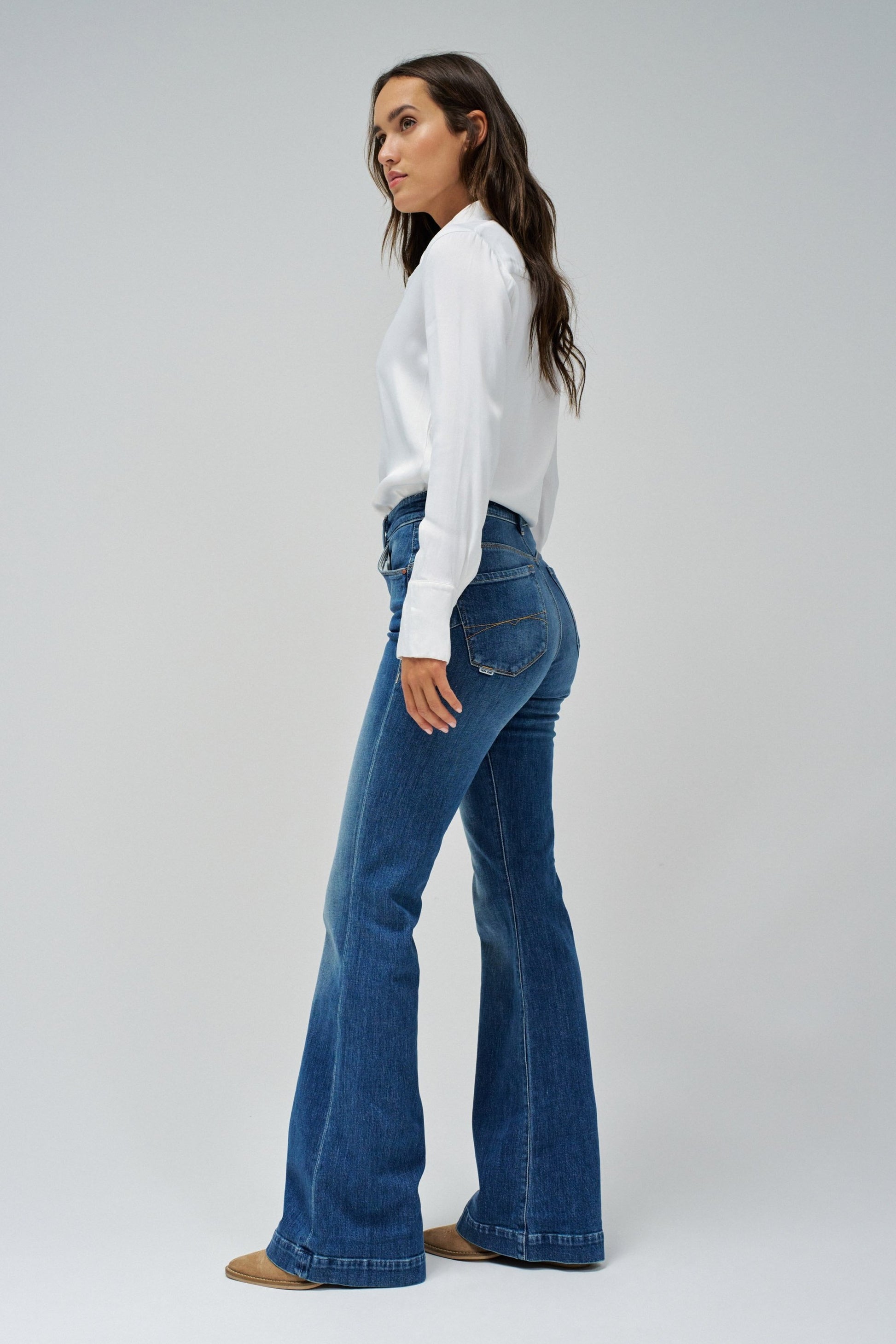 Woman wearing blue flared jeans and a white shirt on a gray background