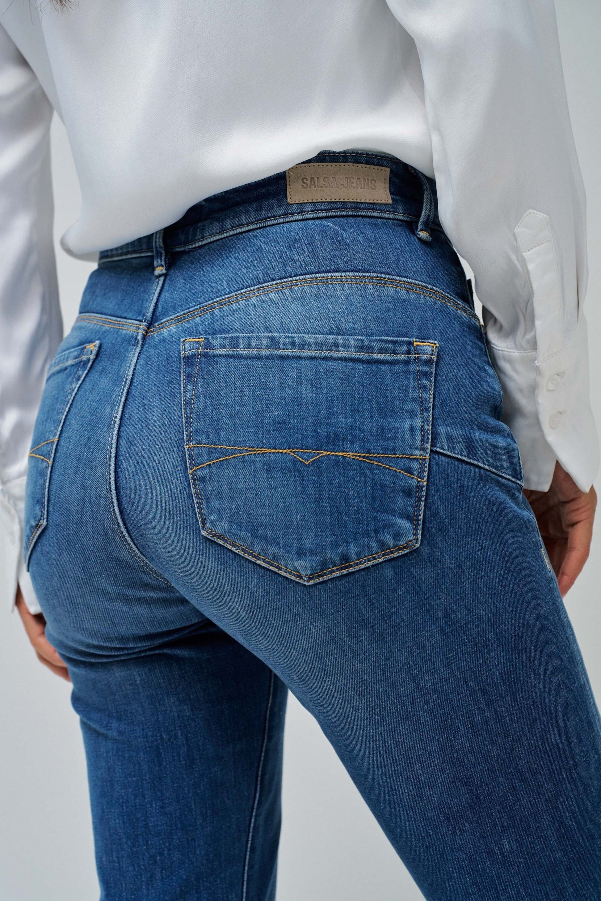 Person wearing blue jeans and a white shirt on a plain background