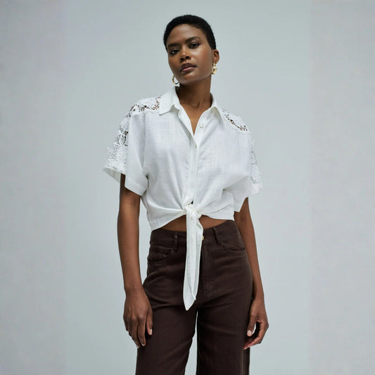 Woman wearing a white blouse with lace details and brown pants on a gray background