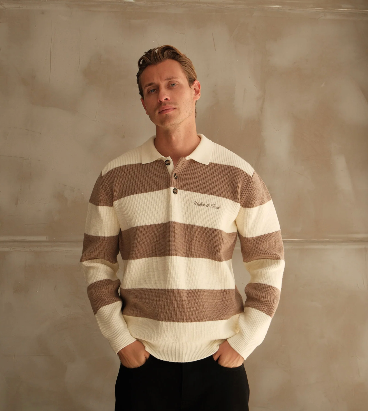 Man wearing a brown and white striped shirt against a textured beige wall