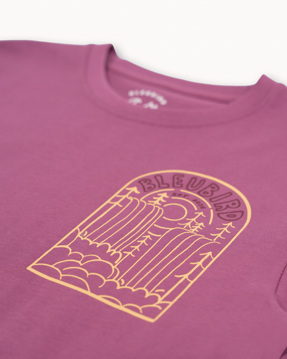 A close-up of a mauve-purple crewneck t-shirt featuring a yellow graphic print of a lighthouse on the front chest, with the brand name 'BLEUSARD' printed above the illustration.