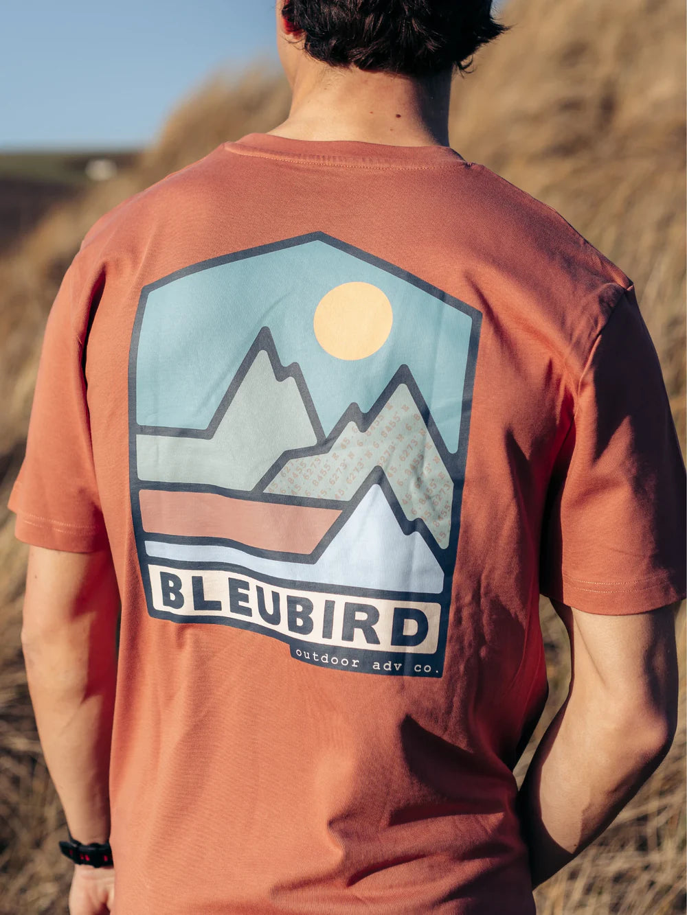 Person wearing a red t-shirt with a mountain graphic and 'BLEUBIRD' branding outdoors.