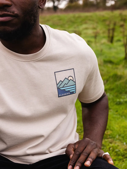 Person wearing a white t-shirt with a mountain logo in a natural setting