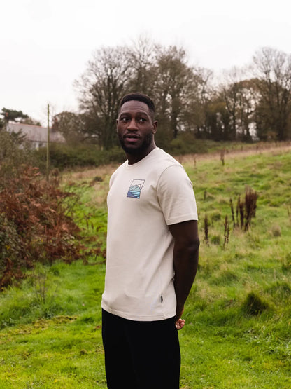 Man wearing a white t-shirt with a logo standing in a grassy field.