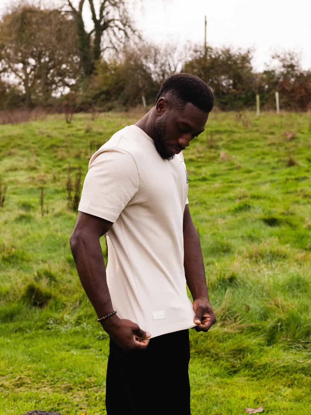 Man wearing a white t-shirt and black pants standing in a grassy field.