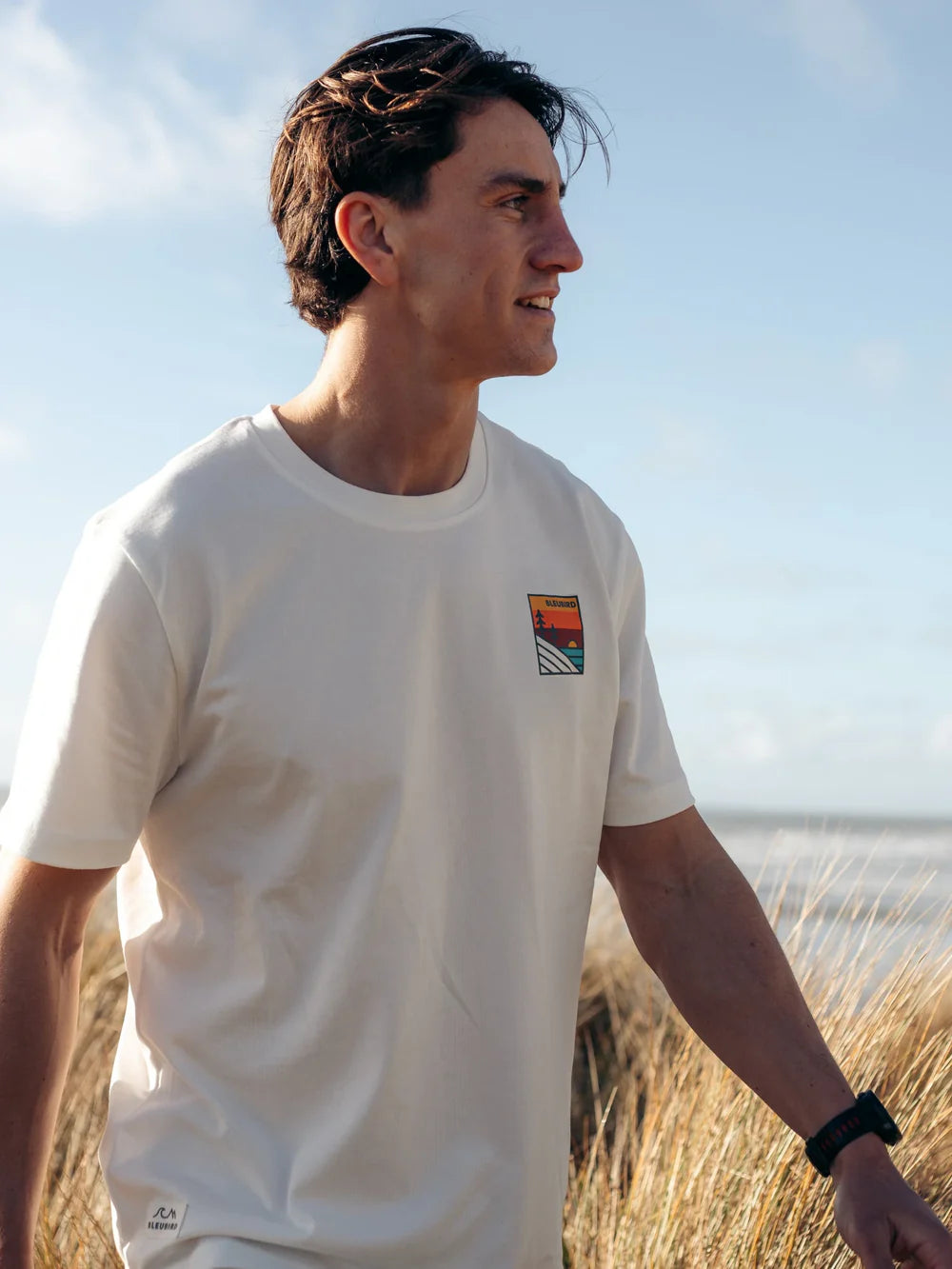 Man wearing a white t-shirt with a colorful logo on a beach