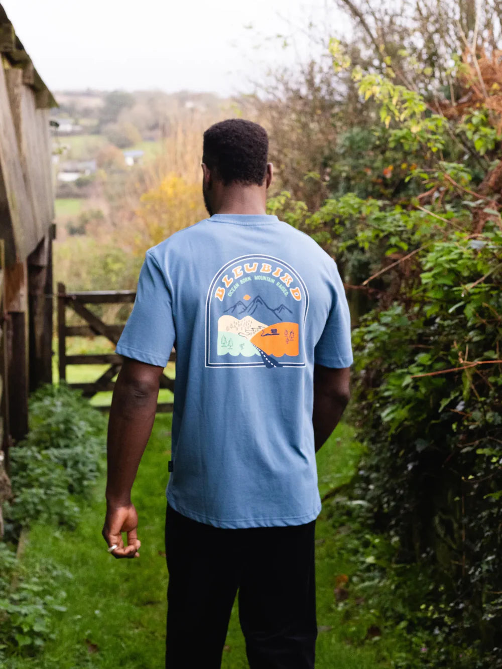 Person wearing a blue t-shirt with a graphic design, standing in a garden.