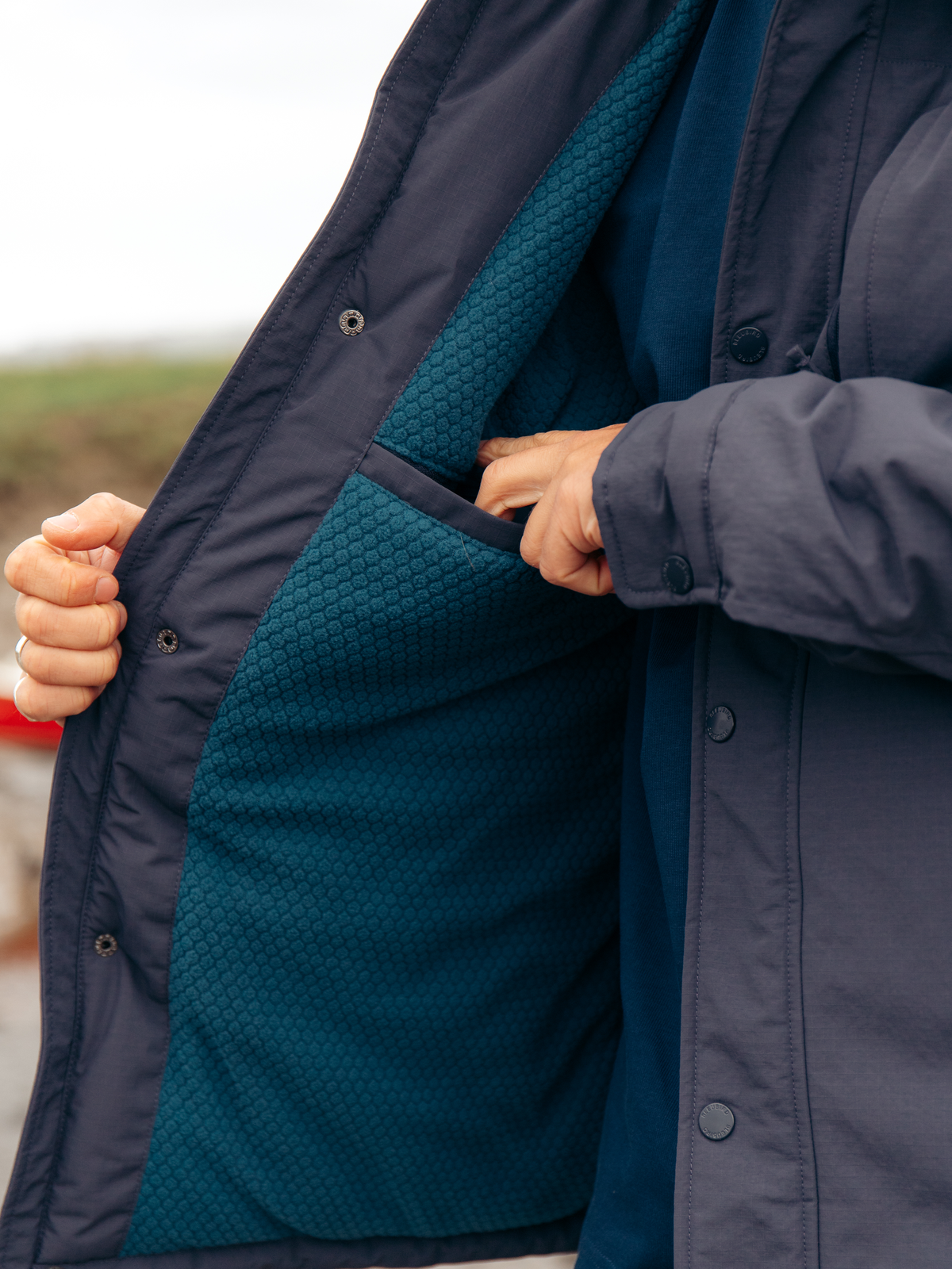 Close-up of a person wearing a dark navy puffer jacket with a teal textured interior lining, showing the pocket and inner lining detail.