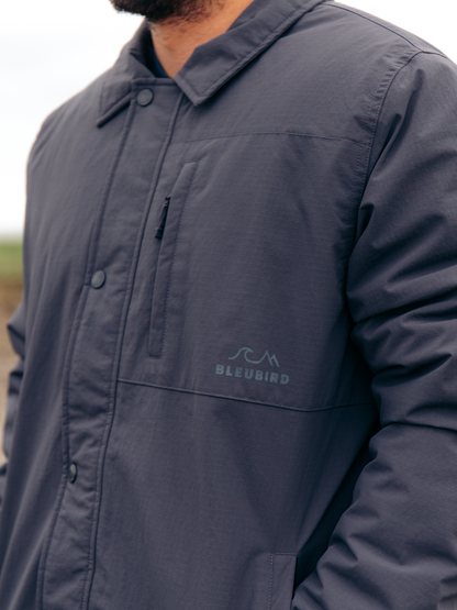 Close-up of a person wearing a dark slate blue button-up overshirt with a subtle embossed Bleubird logo on the left chest.