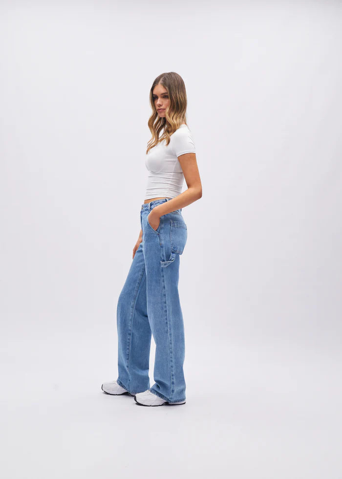 Woman wearing blue jeans and a white top on a plain background
