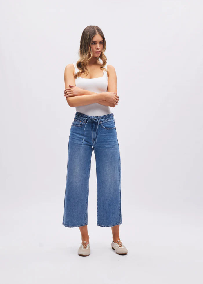 Woman wearing a white tank top and blue jeans on a white background