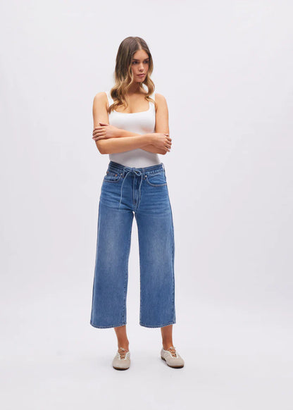 Woman wearing a white tank top and blue jeans on a white background