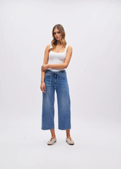 Woman wearing a white tank top and blue jeans on a plain background