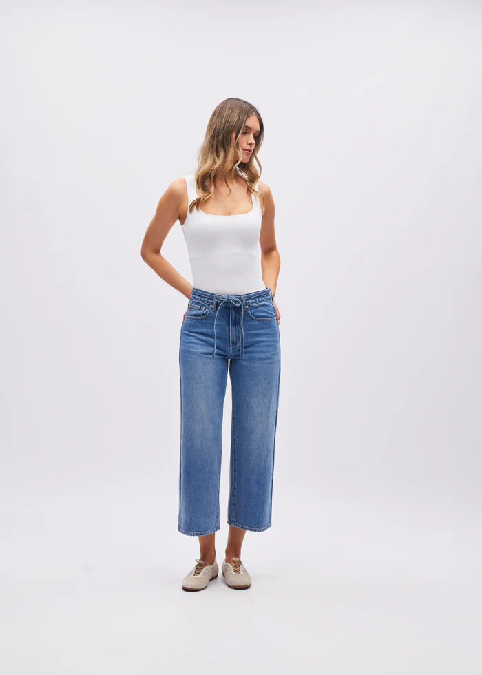 Woman wearing a white tank top and blue jeans on a white background