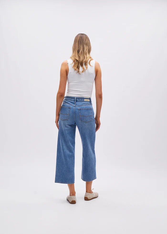 Person wearing blue jeans and a white top on a plain background