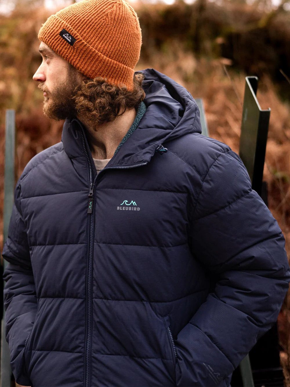 Man wearing a navy puffer jacket with a brand logo, standing outdoors.