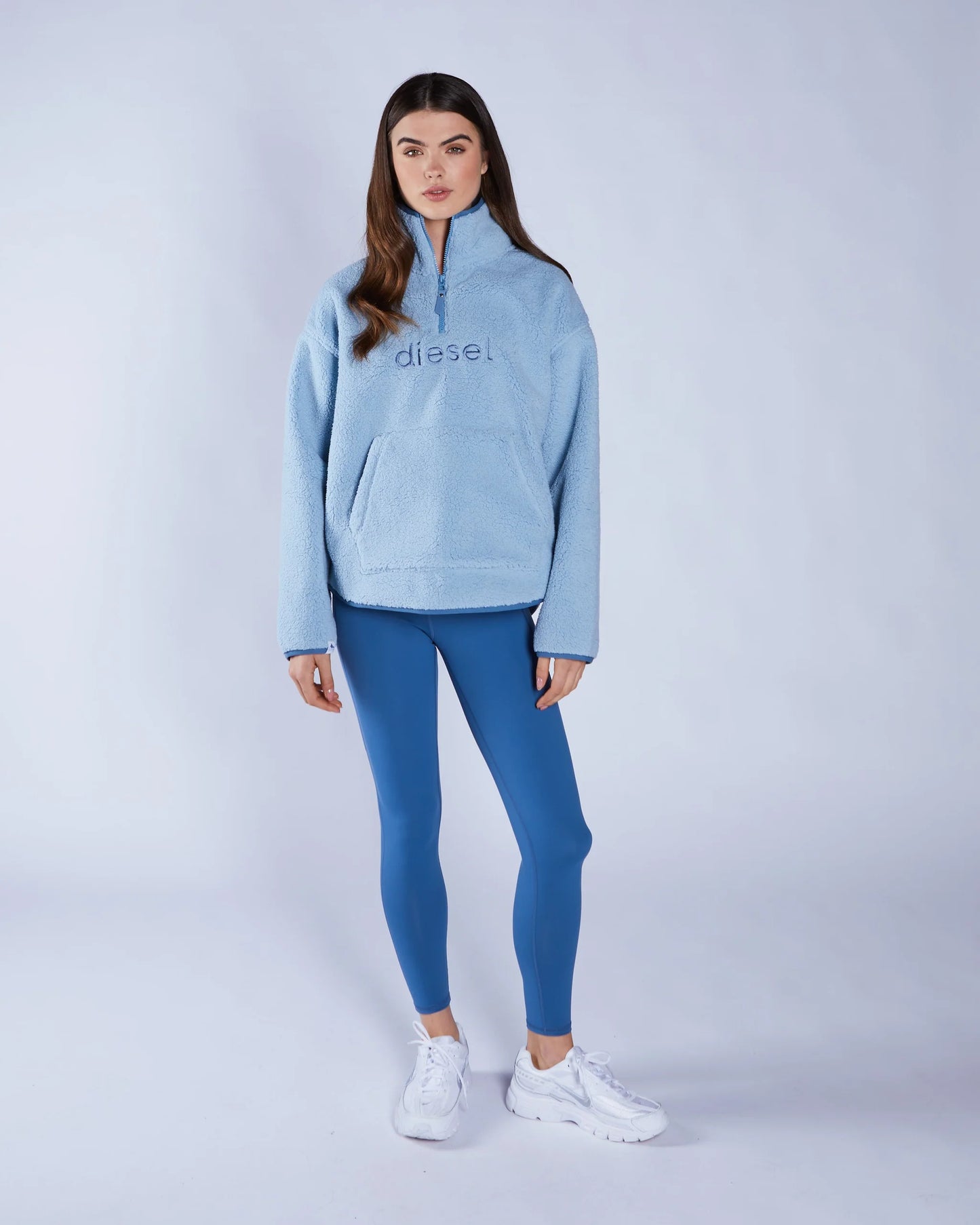 Woman wearing a light blue hoodie and blue leggings with 'Diesel' branding on a white background
