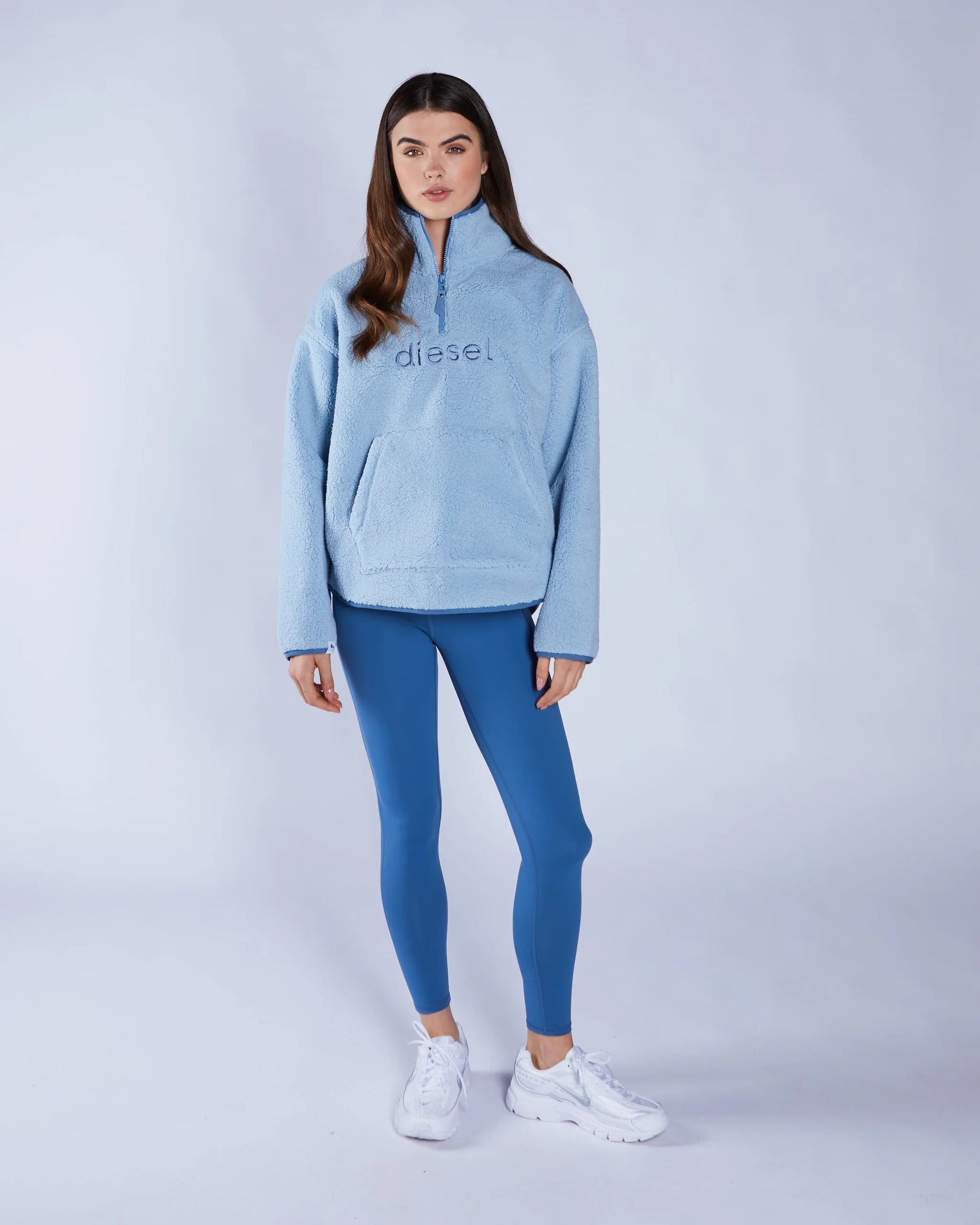 Woman wearing a light blue hoodie and blue leggings with 'Diesel' branding on a white background