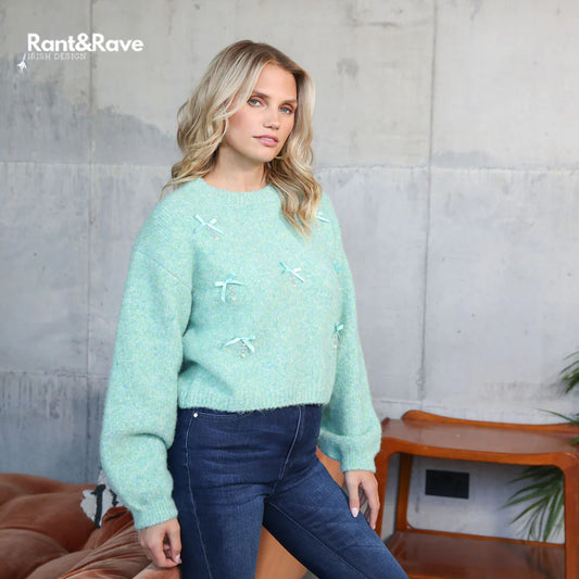 Woman wearing a light blue sweater with white patterns against a gray wall.