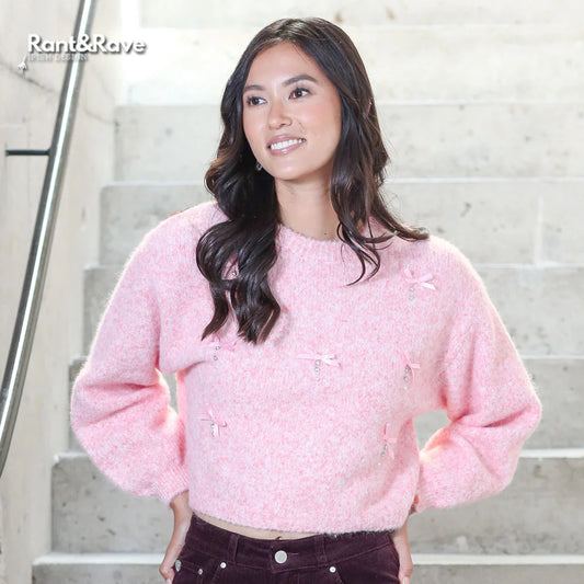 Woman wearing a pink sweater standing on a staircase with 'Rant&Rave' logo.