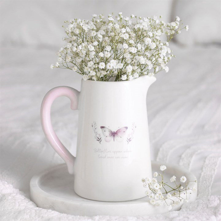 White pitcher with pink handle filled with baby's breath flowers on a white surface.