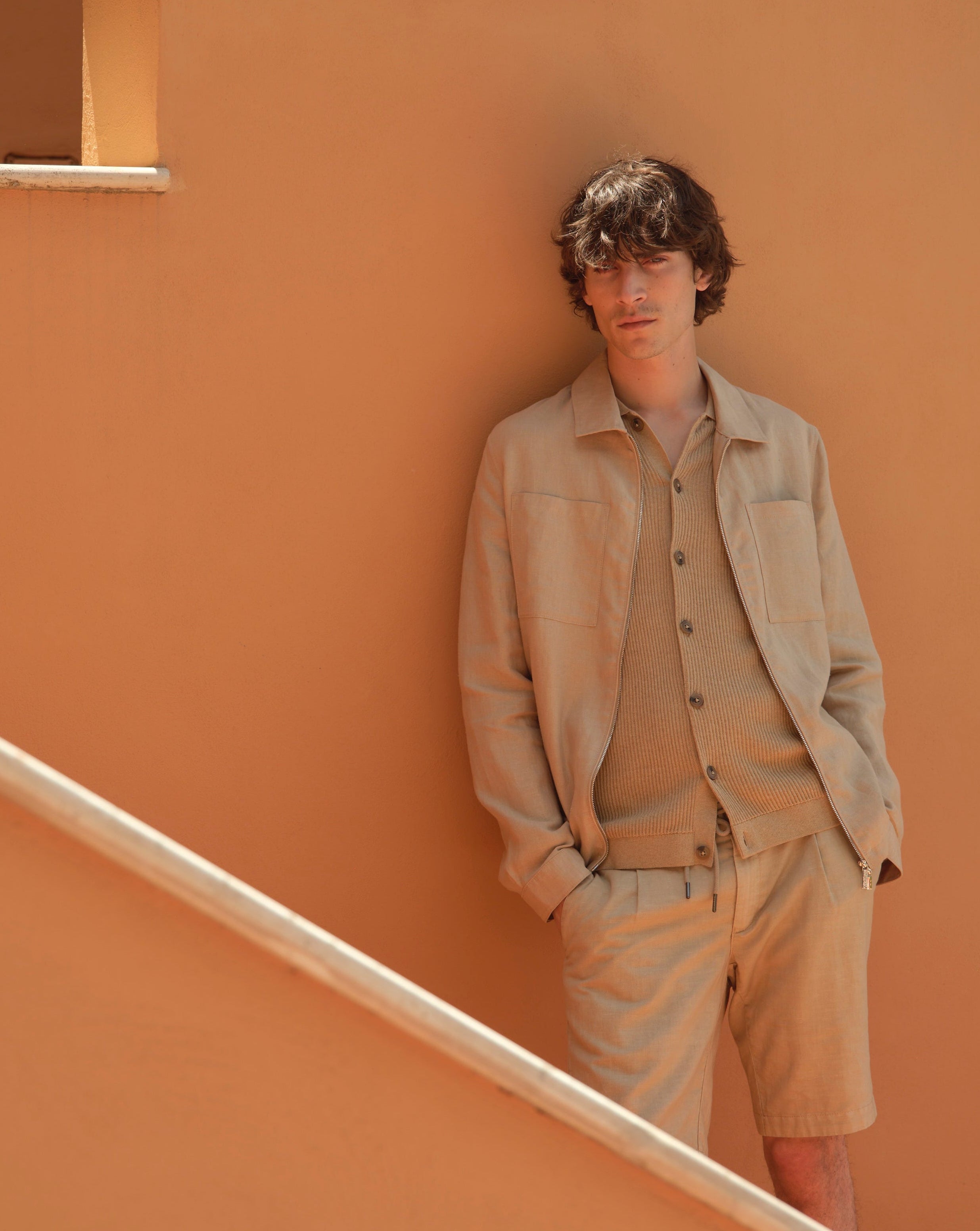 Man in beige suit standing against an orange wall