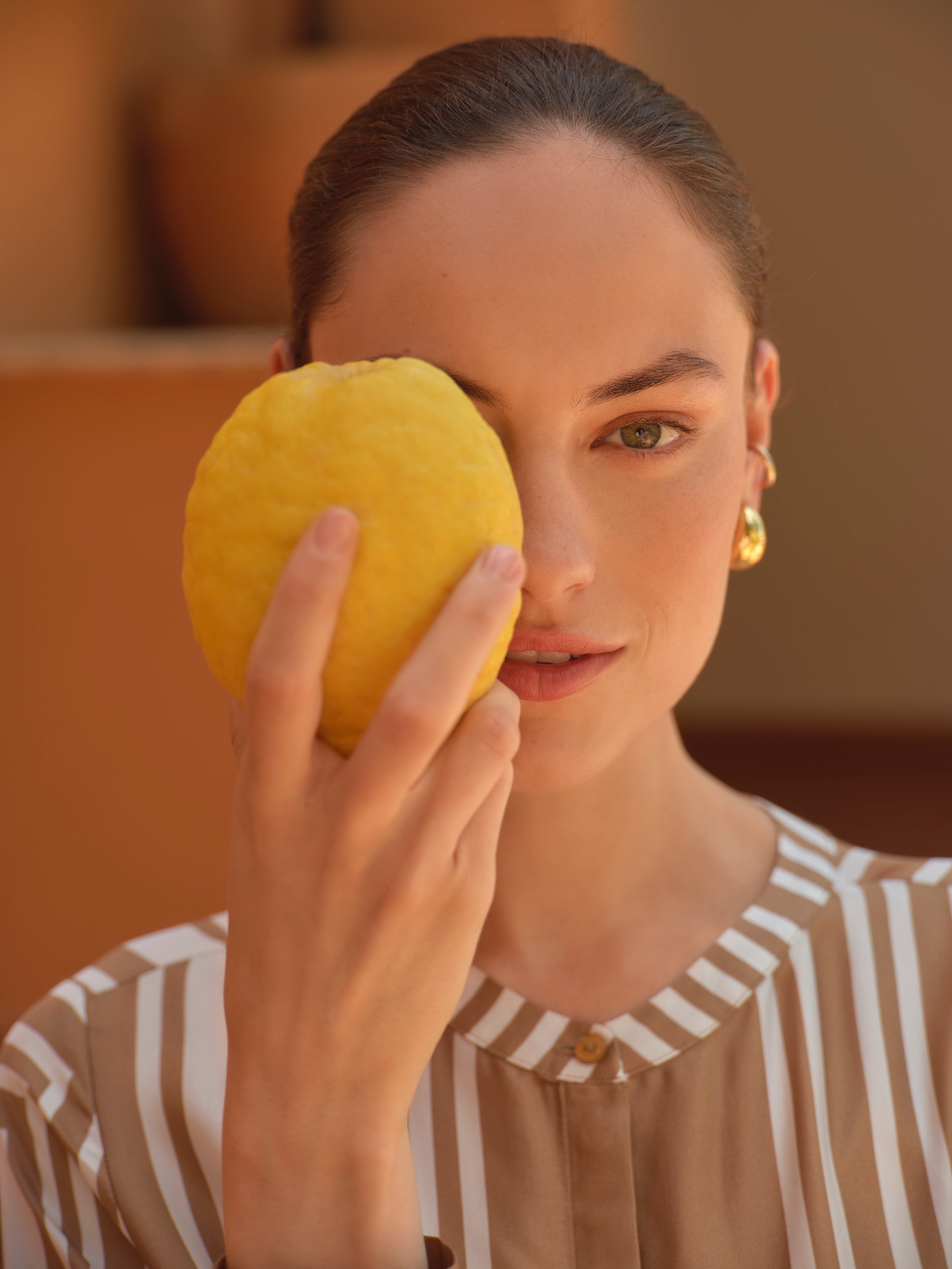 Woman holding a yellow fruit near her face with a blurred background