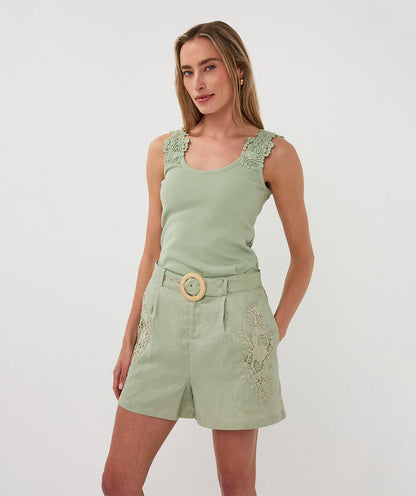 Woman wearing a green sleeveless top and shorts with lace details on a white background