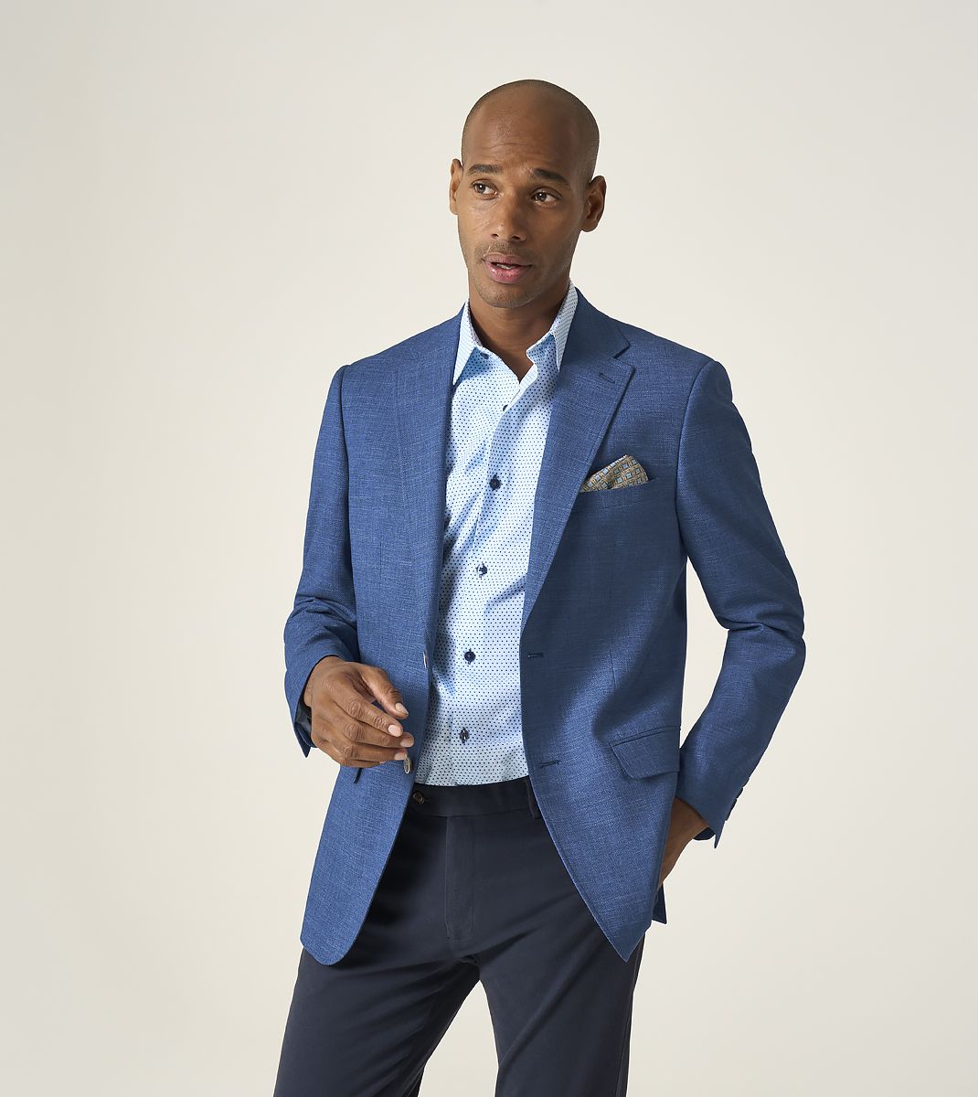 Man wearing a blue suit jacket over a light blue shirt on a plain background