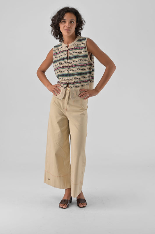 Woman wearing a sleeveless patterned top and beige pants on a gray background