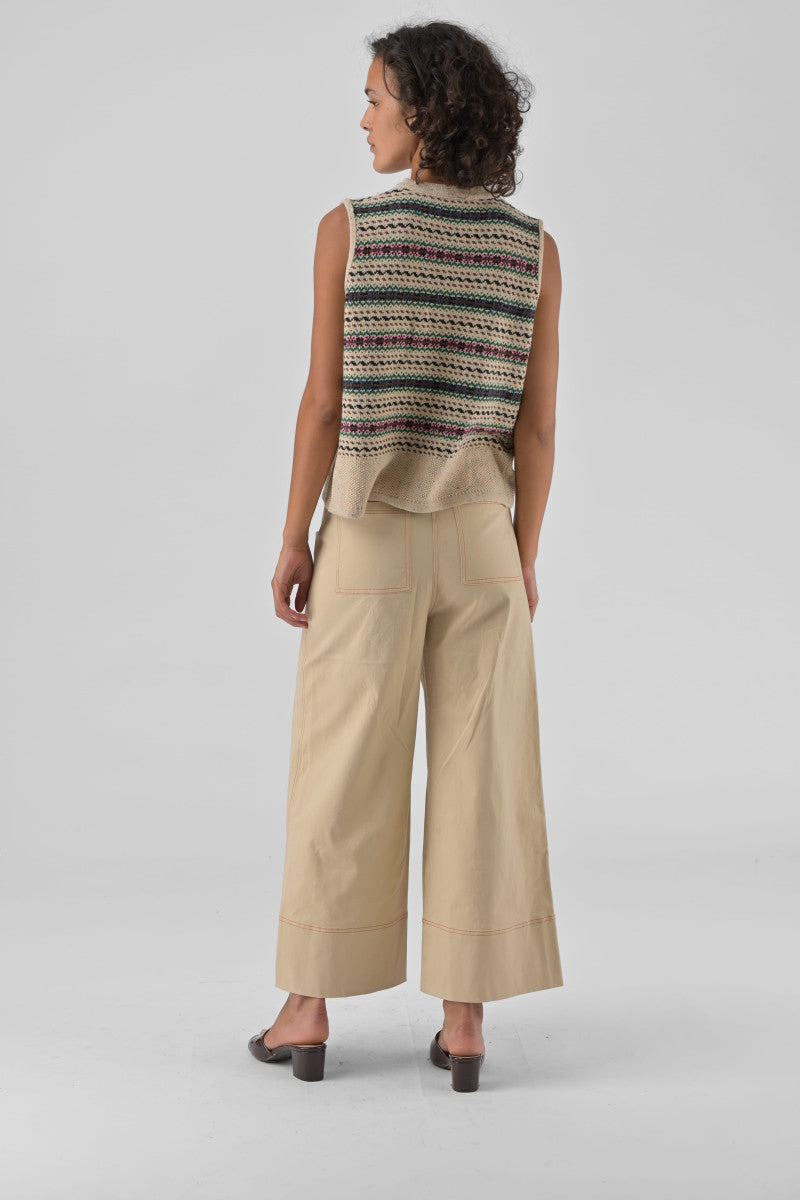 Woman wearing a patterned sleeveless top and beige pants on a plain background